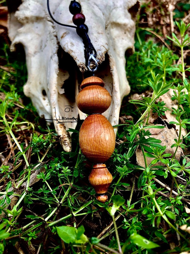 Pendule de radiesthésie en bois tourné Optitourneur, posé sur un lit de mousse et de verdure auprès d’un crâne animal