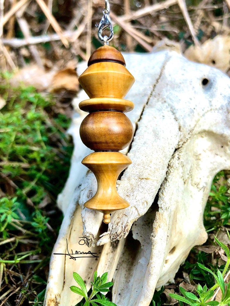 Pendule de radiesthésie en bois clair avec pentagramme argenté, posé sur un crâne animal